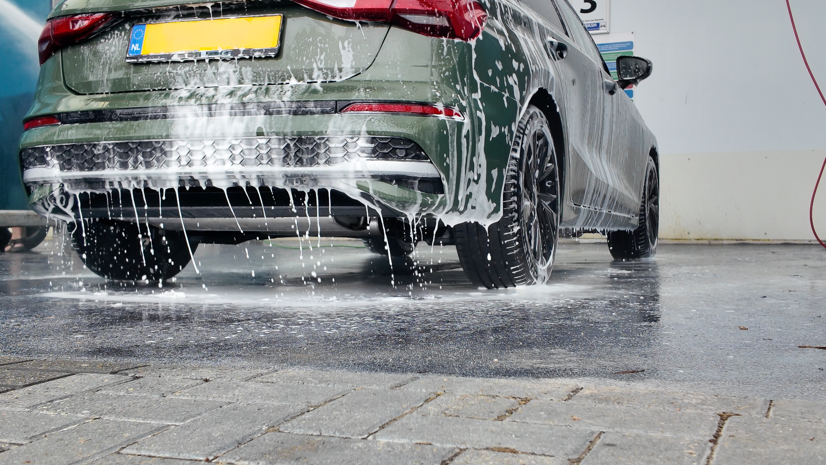 Auto bedekt met schuim en spoelwater tijdens het wassen in een wasbox met klinkervloer